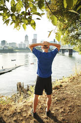 Rear view of sporty man standing by river in city - CAVF71088