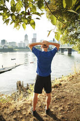 Rückansicht eines sportlichen Mannes, der am Fluss in der Stadt steht - CAVF71088