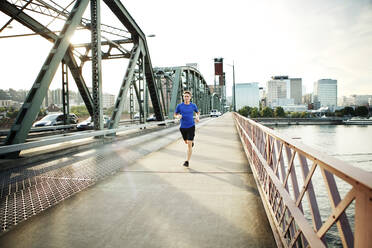 Sportlicher Mann joggt auf Brücke gegen Himmel - CAVF71091