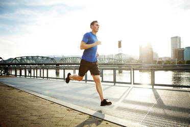 Sportlicher Mann joggt auf der Promenade gegen den Himmel - CAVF71094