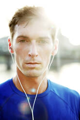 Portrait of sporty young man wearing earphones on sunny day - CAVF71098