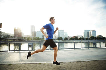 Junger Mann joggt auf der Promenade in der Stadt - CAVF71099