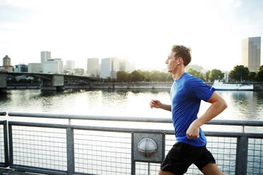 Sportlicher Mann joggt auf der Promenade am Fluss in der Stadt - CAVF71101