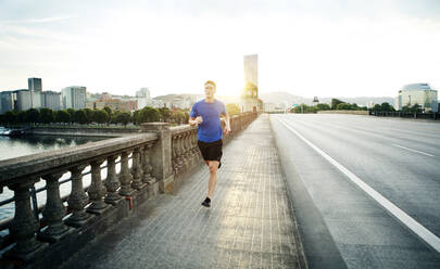 Sporty man jogging on footpath against sky in city - CAVF71107