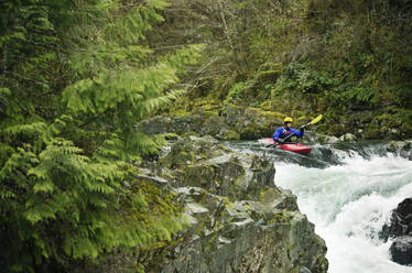 Man kayaking through waterfall in forest - CAVF71113