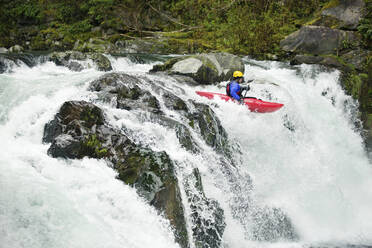 Kayaker paddling through waterfall in forest - CAVF71114