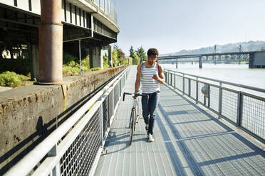 Man using mobile phone while walking with bicycle on promenade - CAVF71129