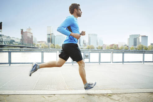 Männlicher Sportler joggt auf der Promenade in der Stadt - CAVF71132