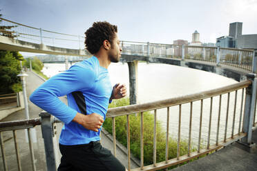 Männlicher Sportler joggt auf einer Brücke in der Stadt - CAVF71133