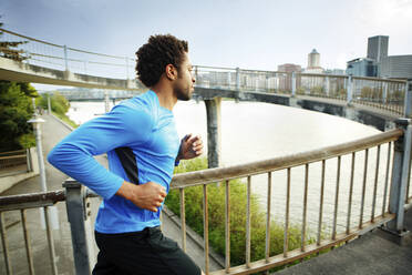 Male athlete jogging on bridge in city - CAVF71133