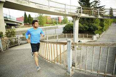 Männlicher Sportler joggt auf einer Brücke - CAVF71134