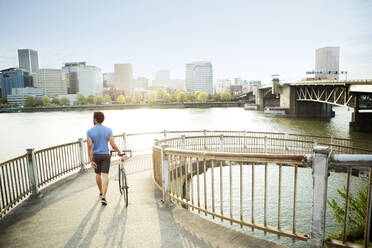 Rückansicht eines männlichen Sportlers, der auf einer Brücke am Fluss in der Stadt läuft - CAVF71144
