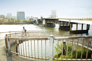 Männlicher Sportler fährt Fahrrad auf einer Brücke in der Stadt - CAVF71145