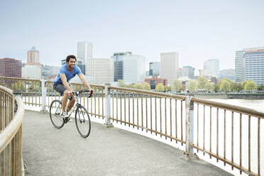 Junger männlicher Sportler fährt Fahrrad auf einer Brücke am Fluss in der Stadt - CAVF71146