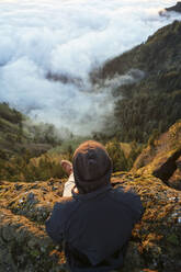 High angle view of hiker sitting on top of mountain and looking at view - CAVF71167