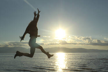 Fröhliche Frau springt am See gegen den Himmel - CAVF71202