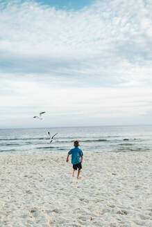 Rückansicht eines Jungen, der am Panama City Beach gegen den bewölkten Himmel läuft - CAVF71241