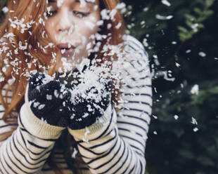 Playful woman blowing shredded papers while standing in backyard - CAVF71281