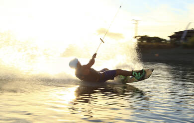 Mann beim Kiteboarden im See während des Sonnenuntergangs - CAVF71321