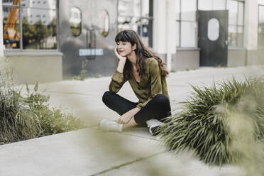 Young smiling woman wearing silk blouse and sitting on the ground - KNSF06967