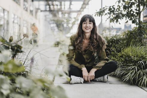 Young smiling woman wearing silk blouse and sitting on the ground - KNSF06968