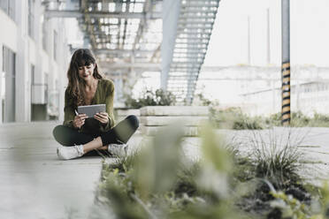 Young smiling woman sitting on the ground and using tablet - KNSF06971