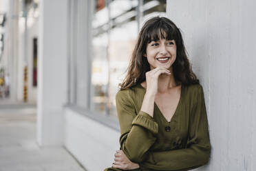 Portrait of smiling brunette woman leaning on a wall, looking sideways - KNSF06977