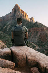 Mann, der auf einem Felsen sitzend die Bergspitze von Zion betrachtet - CAVF71358