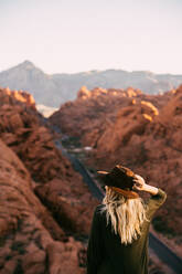 Junges Mädchen betrachtet die herrliche Landschaft, während sie ihren Hut hält - CAVF71364