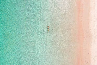 Luftaufnahme einer attraktiven Frau, die am rosafarbenen Strandwasser schwimmt, Padar-Inseln, Indonesien. - AAEF06207