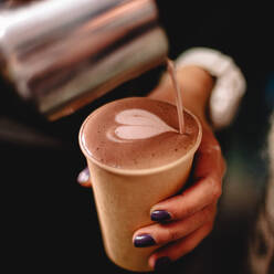 Weibliche Barista gießt Milch in den Kaffee und macht eine Herzform - CAVF71634