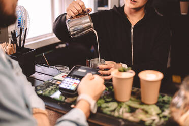 Ein Kunde unterhält sich mit einer weiblichen Barista, während er in einem Café Kaffee kauft - CAVF71640