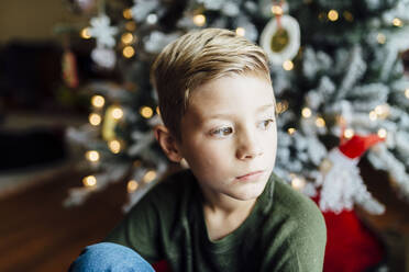 Young boy looking out window next to Christmas tree - CAVF71713