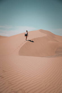 Young Woman hiking on a desert dune leaving footmarks in the sand - CAVF71821