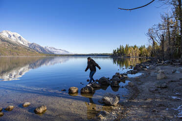 Female jumps on rocks with Grand Tetons on the background - CAVF71829