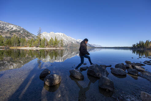 Frau springt auf Felsen mit Grand Tetons im Hintergrund - CAVF71832