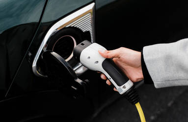 Woman's hand plugging in a charger in an electric car socket - CAVF71929