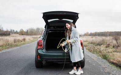 Frau legt ein Ladegerät für Elektroautos in den Kofferraum ihres Autos - CAVF71931