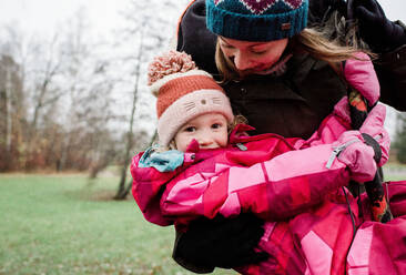 Mother playing with her daughter on a swing outside in winter - CAVF71969