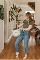 Woman carrying large pot of house plant - ISF23465