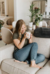 Woman relaxing on sofa with warm beverage - ISF23466