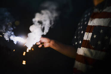 Mittelteil eines Mannes, der ein T-Shirt mit der amerikanischen Flagge trägt und eine Wunderkerze in der Hand hält - CAVF72262