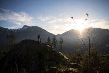 Mann mit Hund bei Sonnenuntergang auf einem Berg stehend - CAVF72321