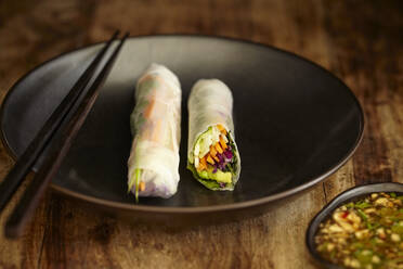 Close-up of spring rolls and chopsticks in plate on wooden table - CAVF72339