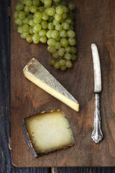 Draufsicht auf Käse mit Buttermesser und Weintrauben auf Schneidebrett - CAVF72345