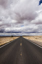 Country road amidst field against stormy clouds - CAVF72390