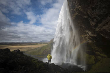 Rückansicht eines Mannes, der auf einem Felsen stehend einen Wasserfall betrachtet - CAVF72417