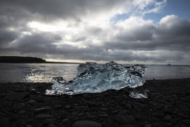 Eisberg auf Felsen am Meer gegen bewölkten Himmel - CAVF72425