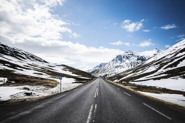 Empty country road by snowcapped mountains against sky during winter - CAVF72430