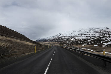 Country road by snowcapped mountains against cloudy sky - CAVF72436